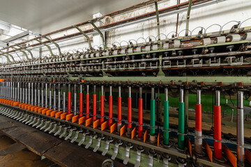 Industrial textile spinning machine with colorful yarn spools inside a factory, automated thread production line. Manufacturing equipment from a traditional wool or cotton mill.