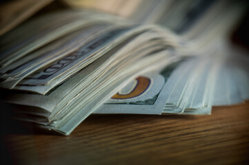 A pile of paper money: American dollars in denominations of $100 and $100 bills. A stack of crumpled bills on a wooden oak table, close-up, blurred, with selective focus.