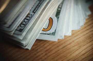 A pile of paper money: American dollars in denominations of $100 and $100 bills. A stack of crumpled bills on a wooden oak table, close-up, blurred, with selective focus.