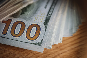 A pile of paper money: American dollars in denominations of $100 and $100 bills. A stack of crumpled bills on a wooden oak table, close-up, blurred, with selective focus.