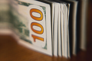 A pile of paper money: American dollars in denominations of $100 and $100 bills. A stack of crumpled bills on a wooden oak table, close-up, blurred, with selective focus.