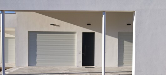Modern house porch entrance with white palster wall and large roller shutters closed. Side light, background and texture.