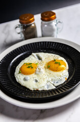 Sunny side up eggs served on black plate with seasoning