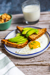 Healthy avocado toast with fried egg on rustic breakfast plate