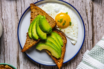 Healthy avocado toast with fried egg on rustic breakfast plate