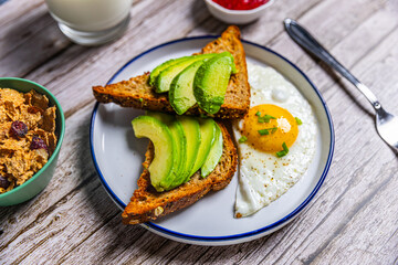 Healthy avocado toast with fried egg on rustic breakfast plate