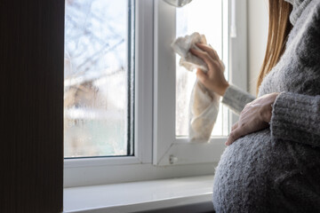 Pregnant woman wipes the condensate from the window glass.