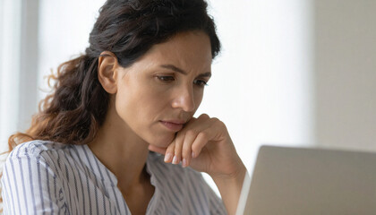 A realistic photo of a upset, worried young adult woman look at the laptop and working remotely at home. Close-up.
