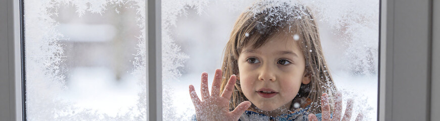 young child face peeks behind frosty windowpane mesmerized falling snowflakes soft warm natural light subtle