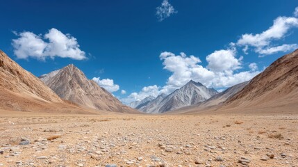 Fototapeta premium Vast Expanses of a Desolate Battlefield Across Barren Land Captured in Majestic Mountain Landscape under Bright Blue Sky and Fluffy Clouds