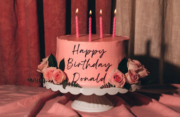 A beautiful pink birthday cake decorated with pink roses and lit candles for donald