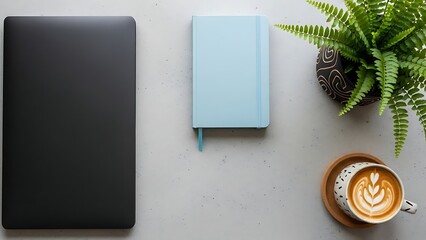 Minimalist desk setup with a closed laptop, a light blue notebook, and a cup of coffee with latte art, next to a potted plant