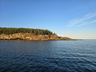 Scenic view of the rocky Acadia National Park coastline and pine forests near Sand Beach from a boat in Bar Harbor, Maine
