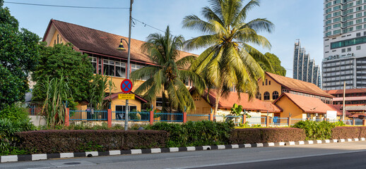 SK. Pendidikan Khas Kg. Baharu, a yellow building with red tiled roof, surrounded by palm trees, with modern high-rises in Kampong Bharu, Kuala Lumpur, Malaysia. © Khaled El-Adawi