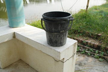 Stacked Black Plastic Buckets on a Concrete Ledge by a Pond