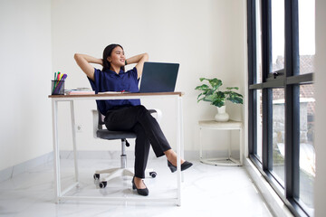Relaxed Asian business woman take break from work put hands behind head lean on comfy chair, enjoy fresh conditioned air in modern office, no stress, fatigue relieve at workplace concept