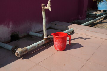 Red Plastic Mug and Water Tap on a Tiled Outdoor Surface