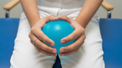 Macro healthcare photography of hands squeezing turquoise therapy ball on clinical blue table, white textile backdrop, rehabilitation exercise, medical wellness concept, bright professional lighting.