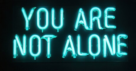 Fototapeta premium Bright turquoise neon sign displays message You Are Not Alone. Dark background emphasizes glowing text, offering comfort, hope.