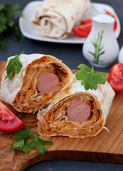Lavash roll with sausage and stewed cabbage on wooden board on gray