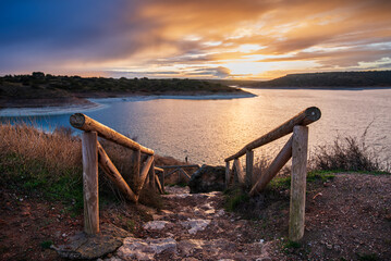 Stairs descending to Pe&ntilde;arroya Reservoir at sunrise, with a bucolic landscape on the horizon, Spain. Scenic early morning lake view.