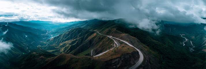 Aerial view of winding road along mountain ridge, cloudy sky, dramatic scenery, cinematic landscape