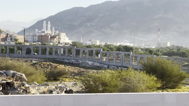 Sacred burial ground of the martyrs (Shuhada) of the historic Badr cemetery and battlefield, featuring a monument engraved with their names, surrounded by a desert mountain town landscape.