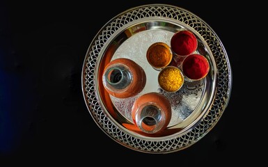 Top view of a traditional Indian puja thali with kumkum, turmeric powder, rice grains and clay kalash arranged on a silver plate over black background