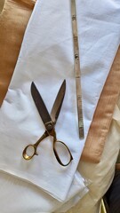 Tailoring tools including scissors and measuring scale placed on folded fabric, representing fashion design, sewing and garment making.