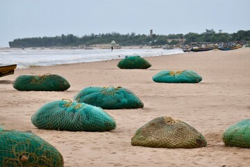 Fishing nets resting on a sandy beach with fishing boats in the background, showing coastal life and traditional fishing industry