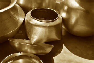 Traditional Indian brass kitchen utensils arranged on the floor with warm sunlight and shadows, showcasing heritage, culture, craftsmanship, and rustic kitchen decor