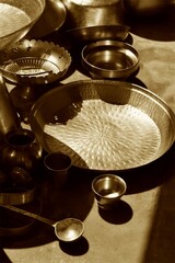 Traditional Indian brass kitchen utensils arranged on the floor with warm sunlight and shadows, showcasing heritage, culture, craftsmanship, and rustic kitchen decor