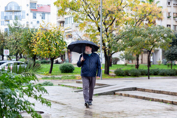 Middle aged man crossing city square with umbrella on rainy autumn day, everyday urban lifestyle