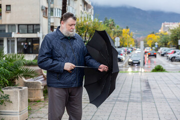 Man standing with umbrella on sidewalk near residential buildings, rainy city lifestyle scene