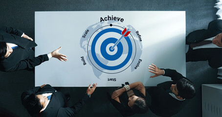 A top-down view of a business meeting featuring a target graphic symbolizes achievement and goal...