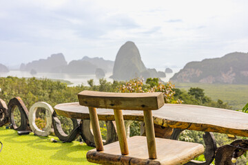 A chair sits beside a round table on a grassy outdoor terrace, offering a panoramic view of rock formations and a distant misty sea. Cheow Lan Lake and Samet Nangshe Viewpoint