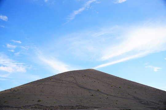 Paisaje minimalista de un cono volc&aacute;nico bajo un cielo azul vibrante con nubes cirros, Lanzarote, Islas Canarias.