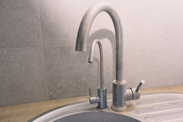Kitchen faucets with heavy limescale and mineral deposits on a stainless steel sink.