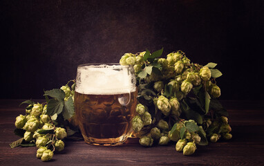 A mug of beer , on a wooden table, with a branch of fresh hops, rustic , no people,