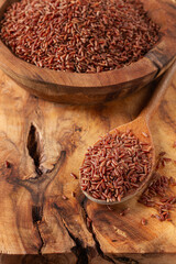 Natural red rice, in a wooden bowl and spoon on a wooden surface in rustic style, top view