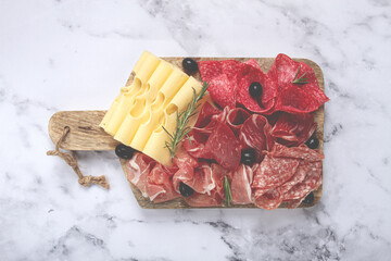 Assorted meat, appetizer, prosciutto, salami and ham, with maasdam cheese and olives, on a wooden board, breakfast, top view, close-up, no people