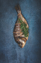 dorado fish, hot smoked, with a sprig of rosemary, tied with a rope, on a blue background, top view, smoked fish, close-up, no people,