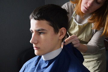 Professional barber covering young man with blue hairdresser cape before haircut