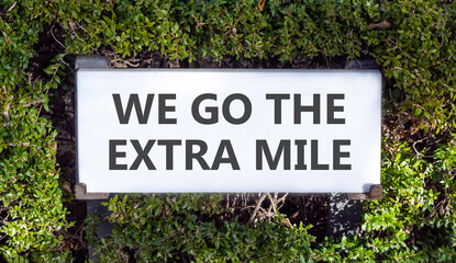 Support, help we go the extra mile symbol. Concept words We go the extra mile on white beautiful road sign. Beautiful green trees background. Business we go the extra mile concept. Copy space.