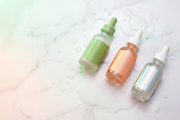 Three colorful glass dropper bottles with liquid on a marble surface showcasing beauty products