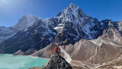 Adventurer celebrates achievement amidst majestic snow-capped peaks and vibrant turquoise glacial lake, capturing the breathtaking beauty of the high mountains