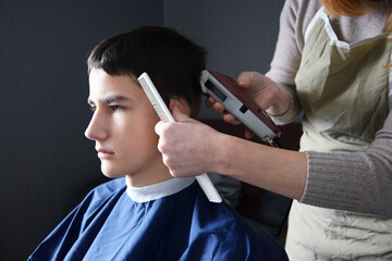 Close up of hairdresser using professional electric clipper and white comb for boy's haircut