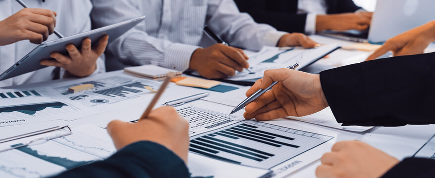 A diverse business team engaged in reviewing financial reports and data visualizations in a modern office. Collaboration and analysis drive insights for strategic decisions. SACTR - Powered by Adobe