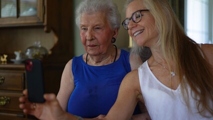 Elderly woman and her daughter spend time looking at pictures and making video calls while sitting together in a home setting