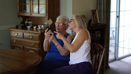 Senior woman and her daughter share a moment while looking at pictures and making video calls in a comfortable home setting